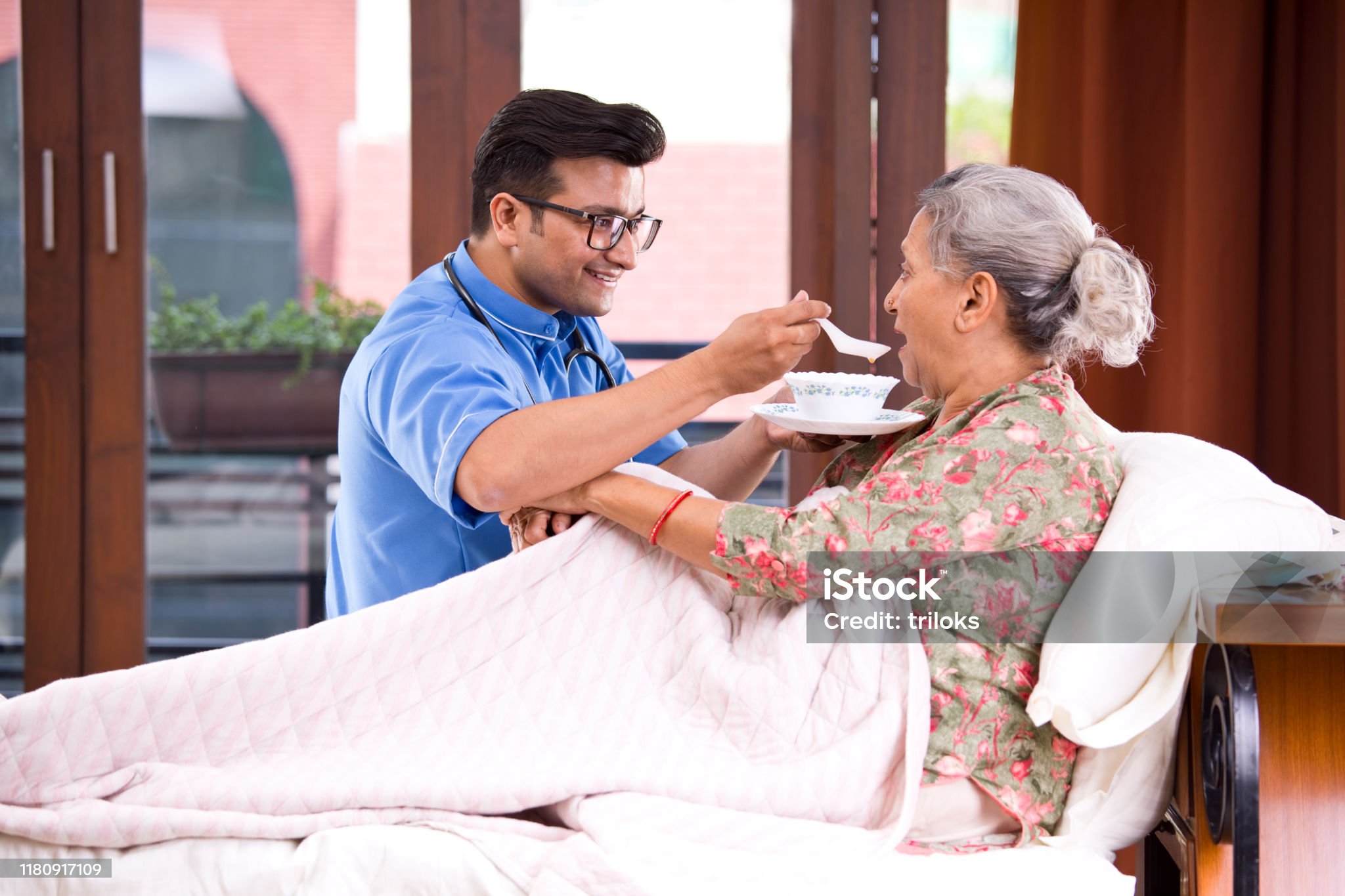 male nurse feeding food to senior patient on bed
